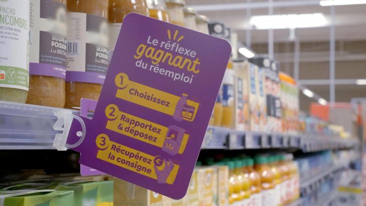 Une étiquette « Le Réflexe gagnant du réemploi » installée dans un rayon de supermarché devant des bouteilles consignées